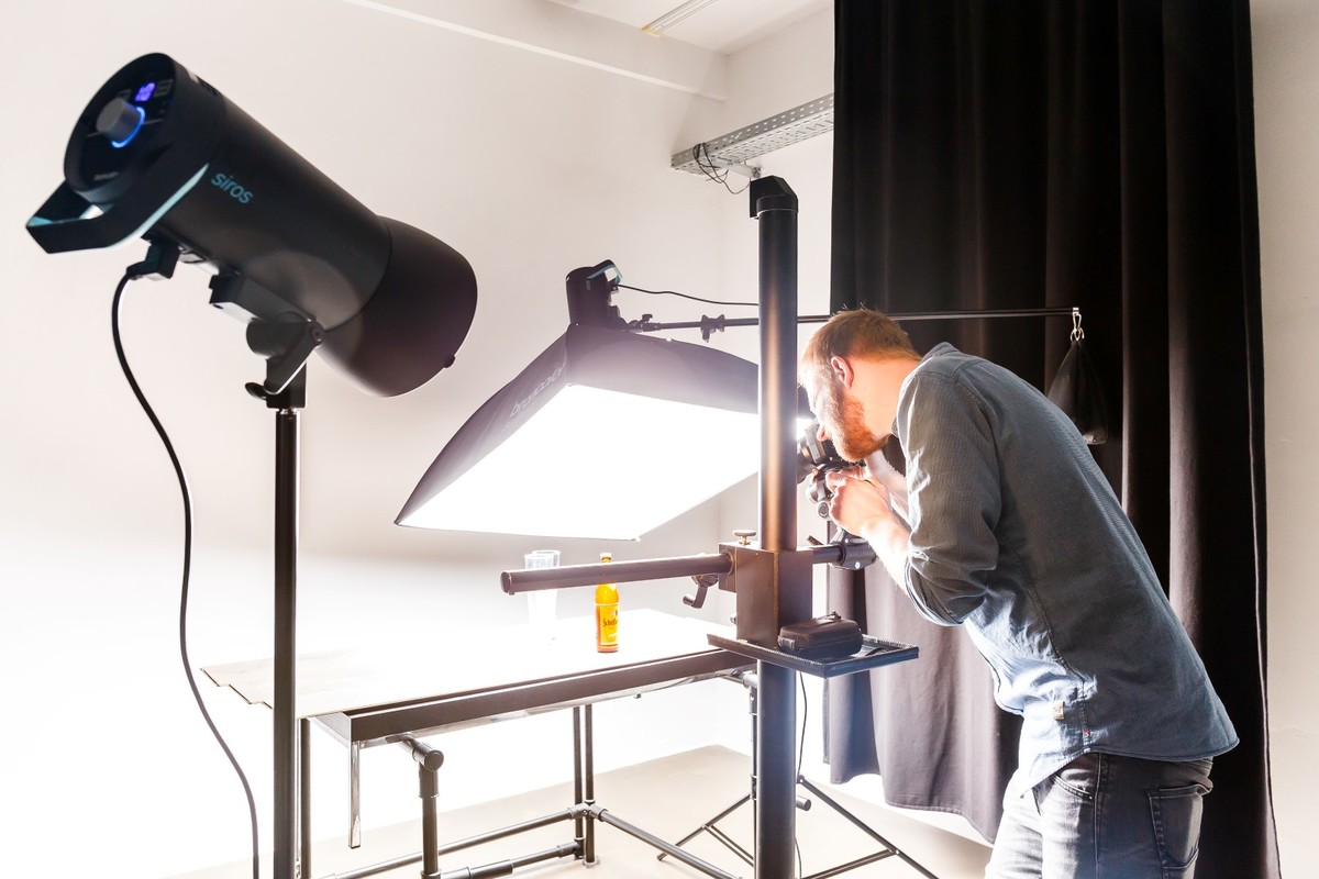 Person an einem beleuchteten Aufnahmetisch mit Studiolicht und Reflektor.