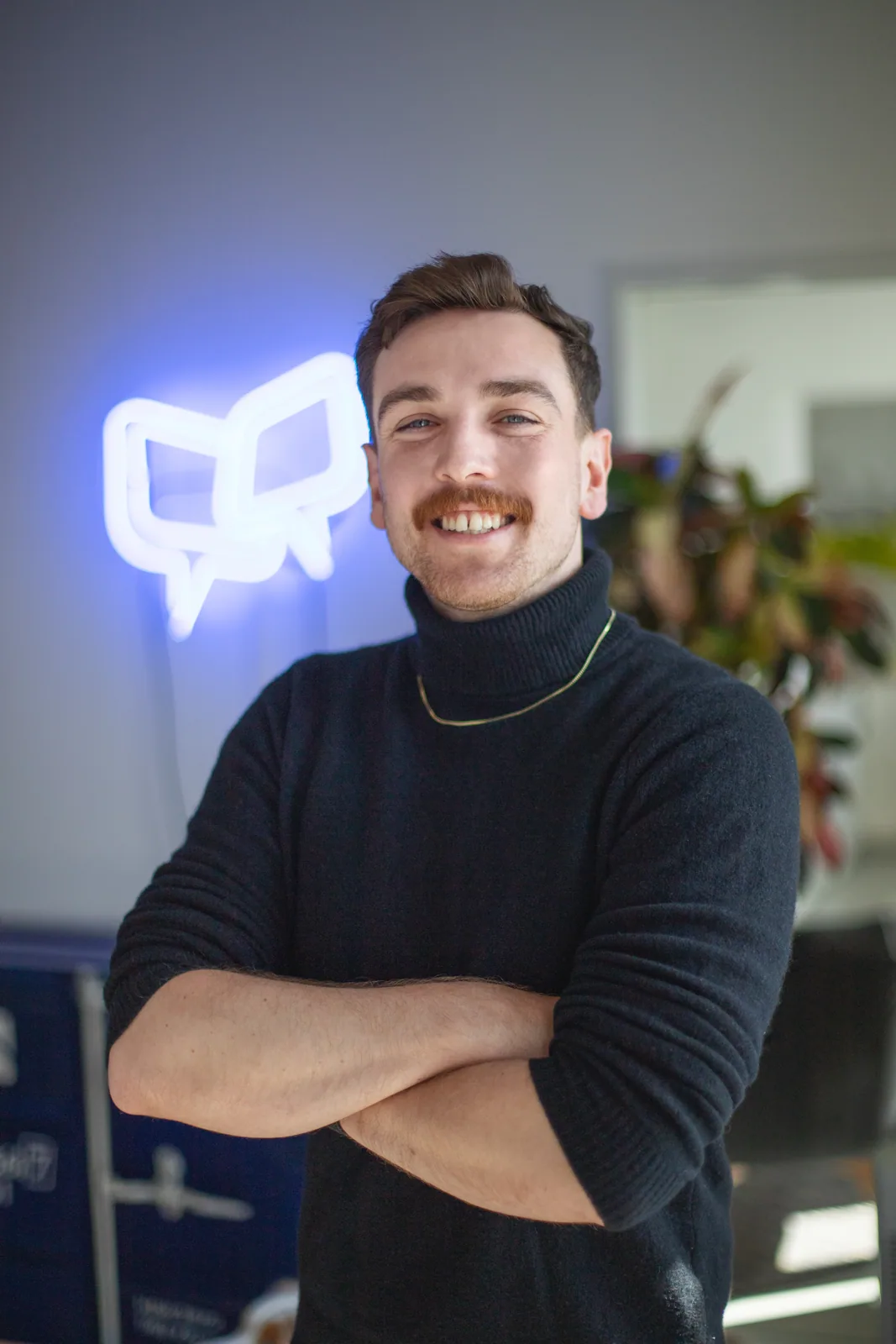Porträt einer lächelnden Person in einem dunklen Pullover vor dem leuchtenden OnlineDialog-Sprechblasenlogo.